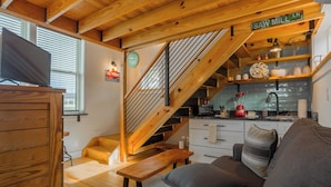 Un salon chaleureux avec un escalier en bois, une cuisine équipée d’un mixeur et une pancarte indiquant « Saw Mill Ln ».