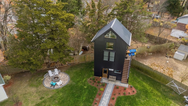 Une maison moderne à l’extérieur sombre, dotée d’un patio circulaire aménagé avec du mobilier d’extérieur et d’une petite terrasse.