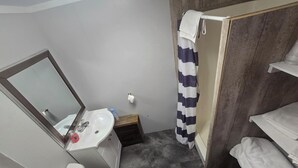 A compact bathroom with a white sink, a mirror, a toilet, and a shower area with a striped curtain.