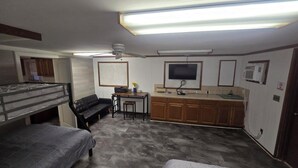 A compact room with bunk beds, a small kitchenette, a television, and a ceiling fan.