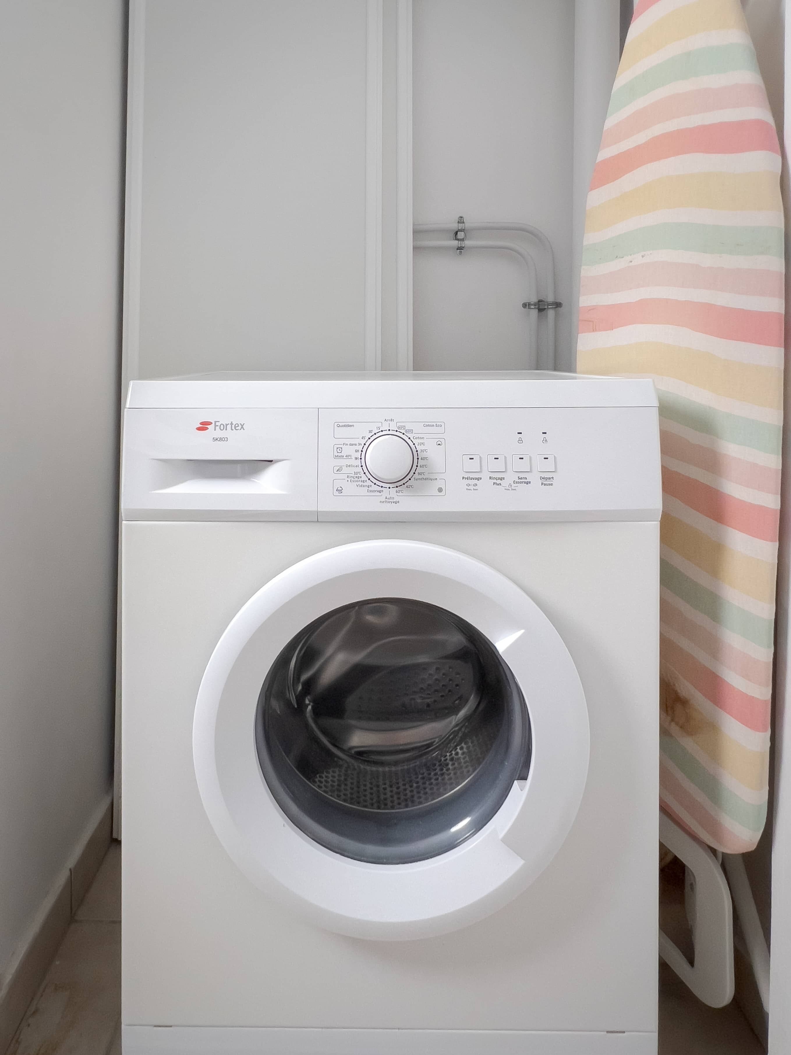 A front-loading washing machine with a control panel, a door, and a striped towel hanging nearby.