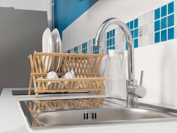 A kitchen sink with a dish rack holding white dishes, a faucet, and a tiled backsplash with blue and white tiles. - Crystal Beach Suite (Saint-François)