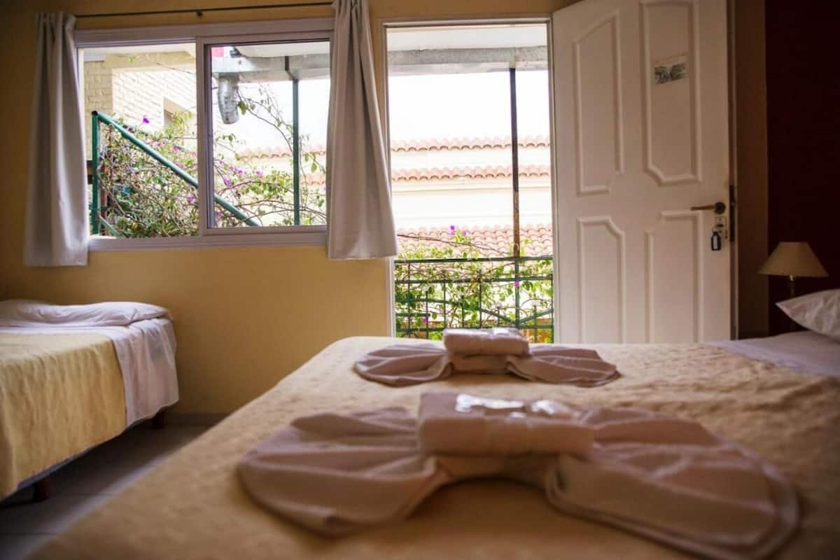 Ein Hotelzimmer mit zwei Betten, einem Fenster mit Vorhängen und Blick auf einen Garten.