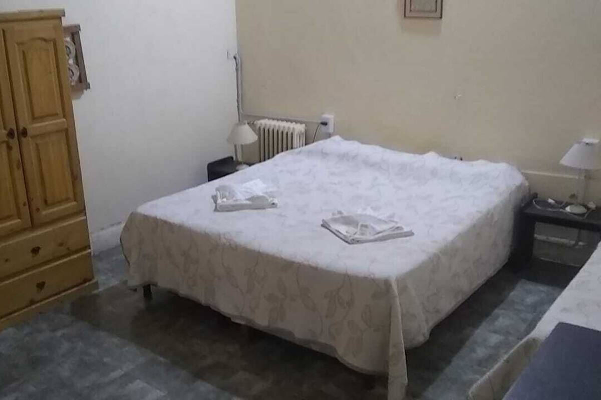 Ein Schlafzimmer mit einem Bett, einem Holzschrank, einem Heizkörper und einem Nachttisch mit einer Lampe.