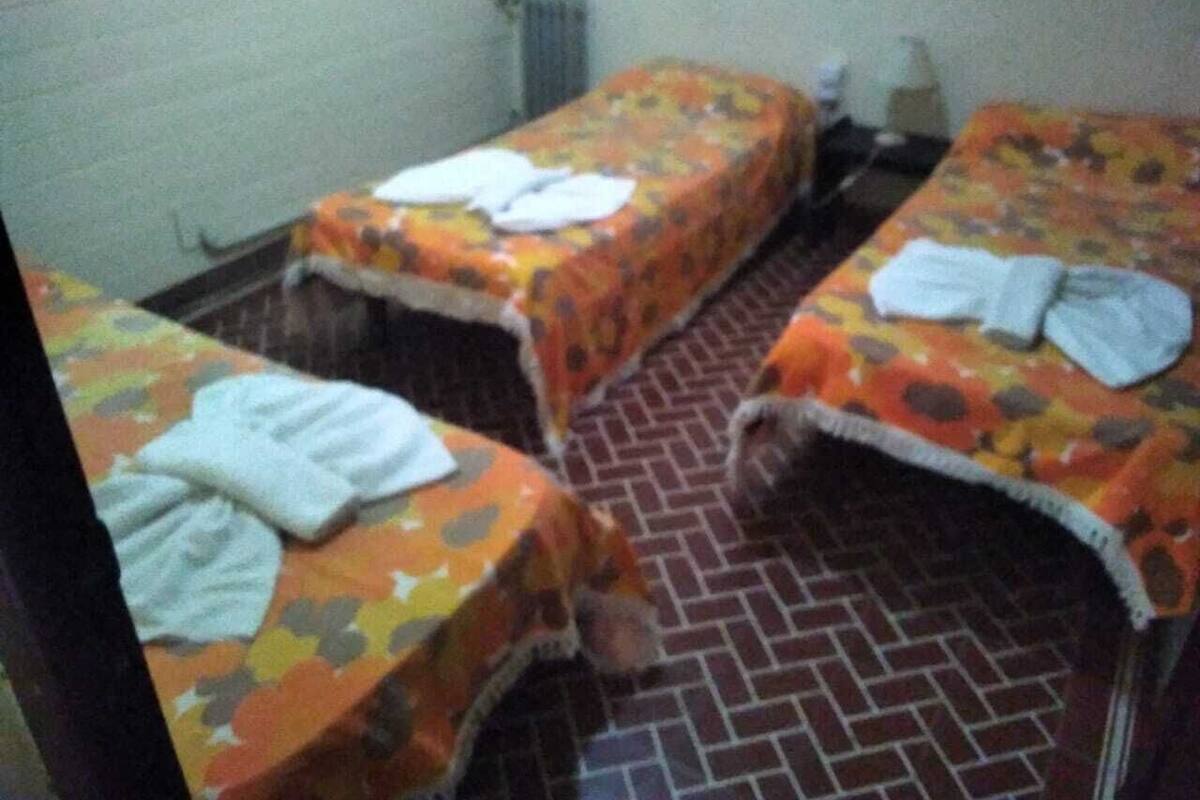 Ein Zimmer mit zwei Betten, jeweils mit floralem Überwurf und weißen Handtüchern. Der Boden ist mit einer Ziegeloptik gefliest.