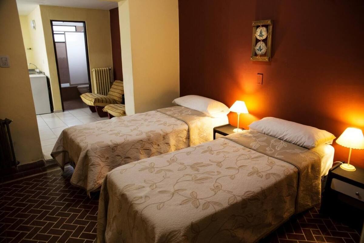 Ein Hotelzimmer mit zwei Betten, einem Sessel, einem Nachttisch mit Lampe und einer Wanduhr.