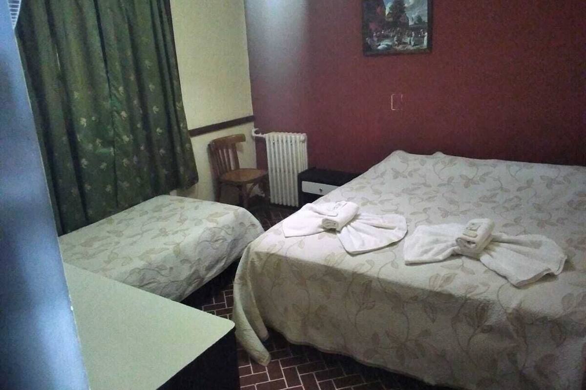 Ein Zimmer mit zwei Betten, einem Heizkörper, einem Sessel und einem kleinen Tisch.