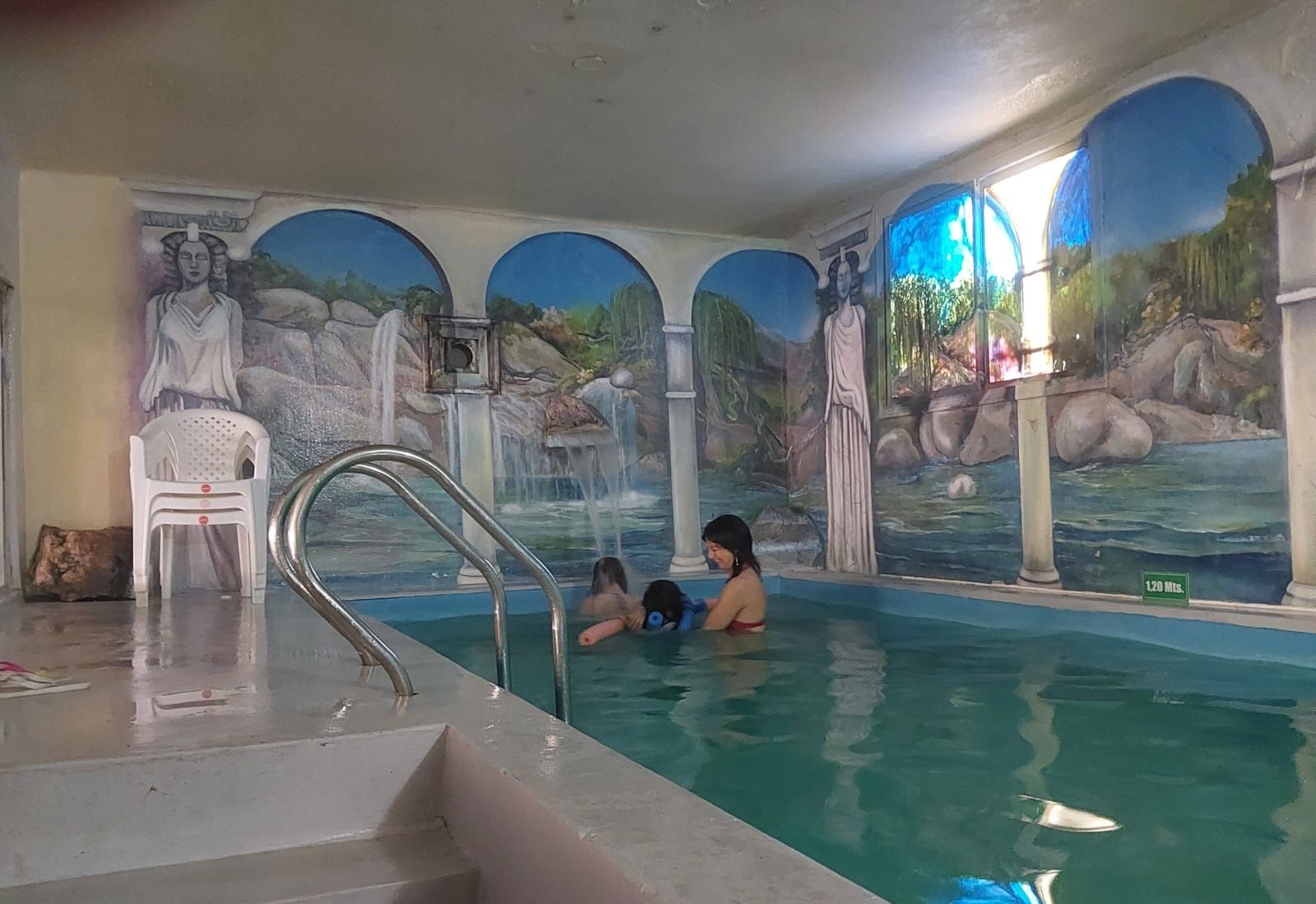 An indoor swimming pool with murals, a lifeguard chair, and a sign indicating a 120-minute session.