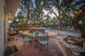 Une terrasse extérieure avec une table ronde et des chaises, un barbecue et des guirlandes lumineuses.