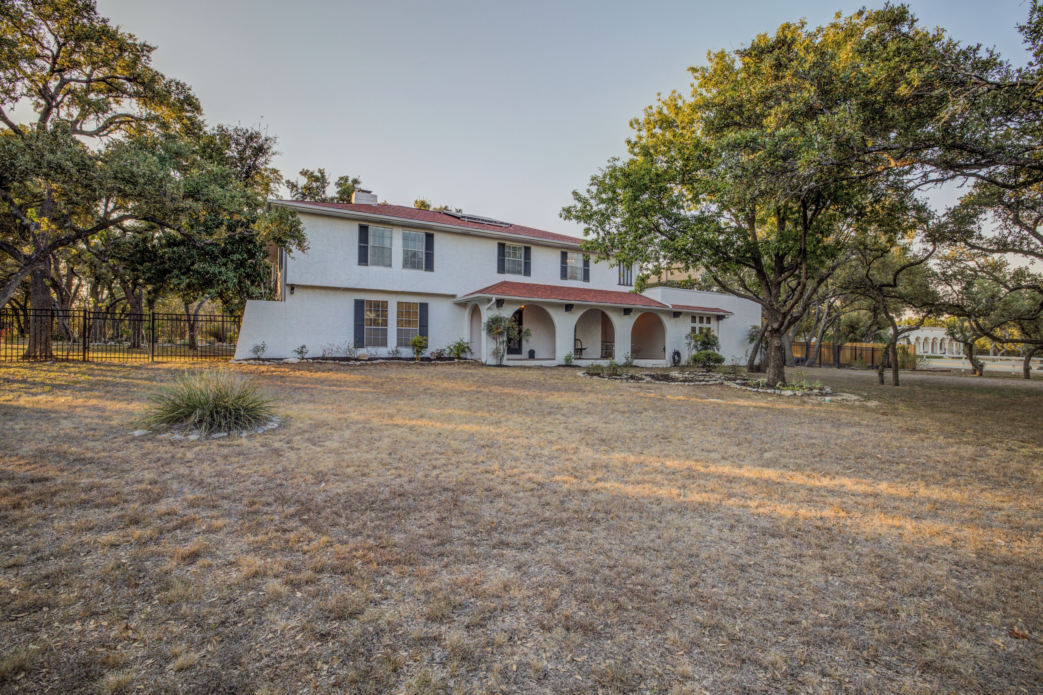 A two-story house with a red roof, a front porch with columns, and a fenced yard.