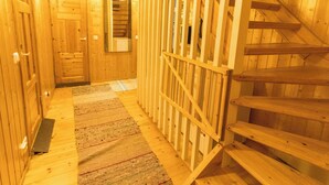 Un couloir intérieur aux murs en bois, avec un escalier, un miroir et un tapis à motifs.