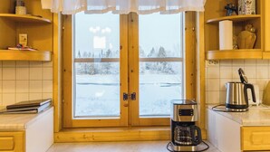 Une cuisine avec des meubles en bois, une machine à café et une vue sur un paysage enneigé par la fenêtre.