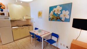 A compact kitchen with a dining area, a TV, and a painting of flowers on the wall.