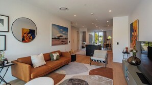 A modern living room with a brown leather sofa, a white armchair, and a dining area with a table and chairs. - Malthouse Lane City Apartment 4 with Stunning Hill Views in Nelson CBD (Nelson)