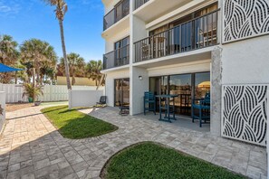 A multi-story building with balconies, a patio area with outdoor furniture, and a white picket fence.