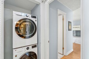 Un lavadero con dos lavadoras apiladas, una puerta que da a otra habitación y un cuadro en la pared.