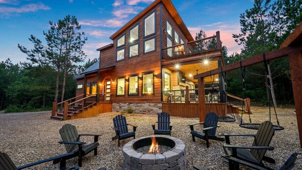 Una cabana de fusta de dos pisos amb una llar de foc i seients Adirondack al jardí davanter.