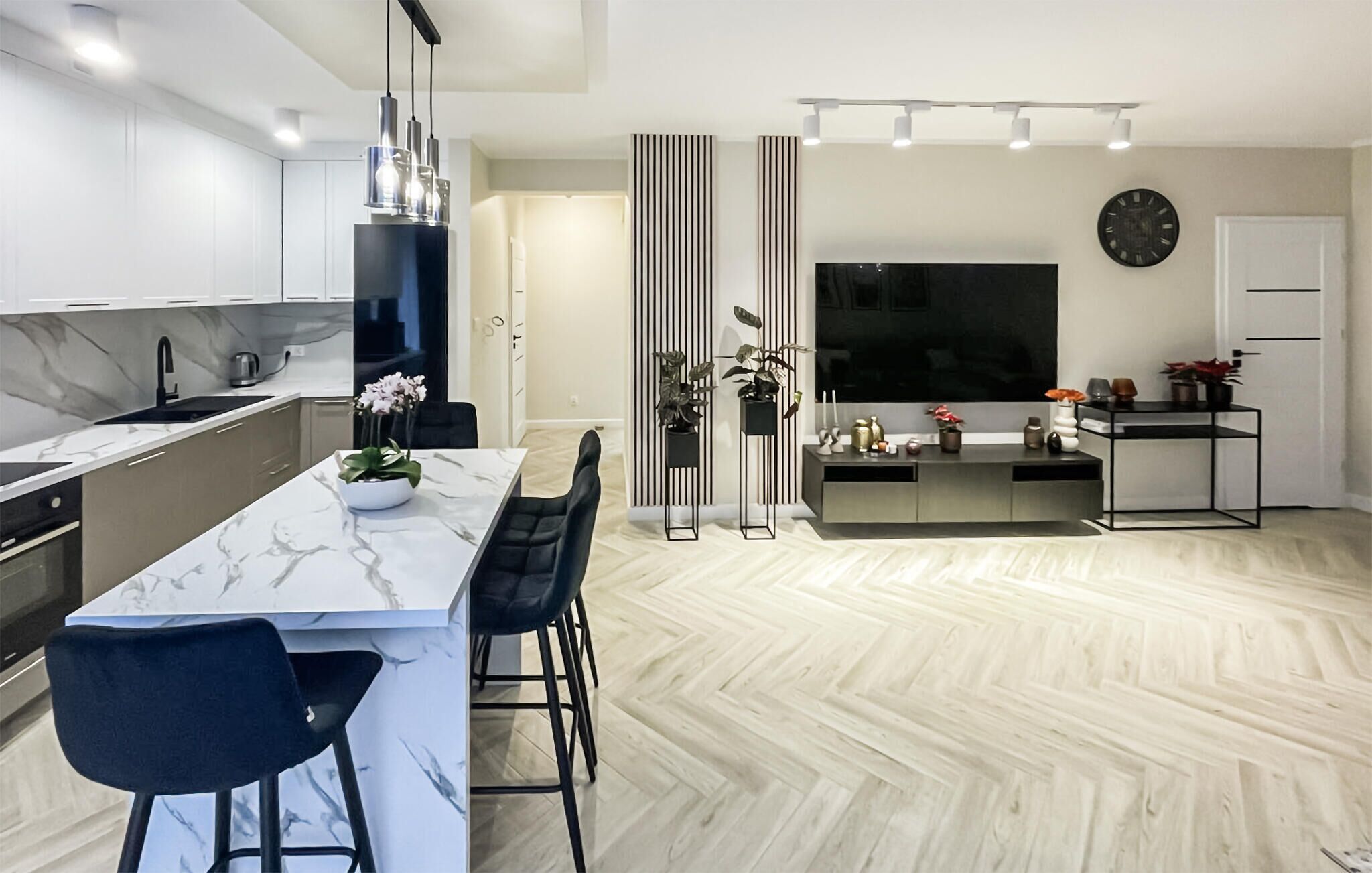A modern kitchen with a marble countertop, black chairs, and pendant lighting.