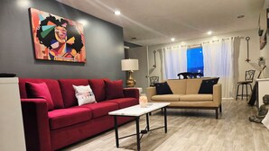 A living room with a red sofa, beige sofa, and a white coffee table. There is a painting on the wall and a Buddha statue on the floor.