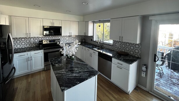 A modern kitchen with white cabinets, black countertops, and a central island. - Charming Broomfield Retreat: Modern Comforts & Prime Location
 (Broomfield)