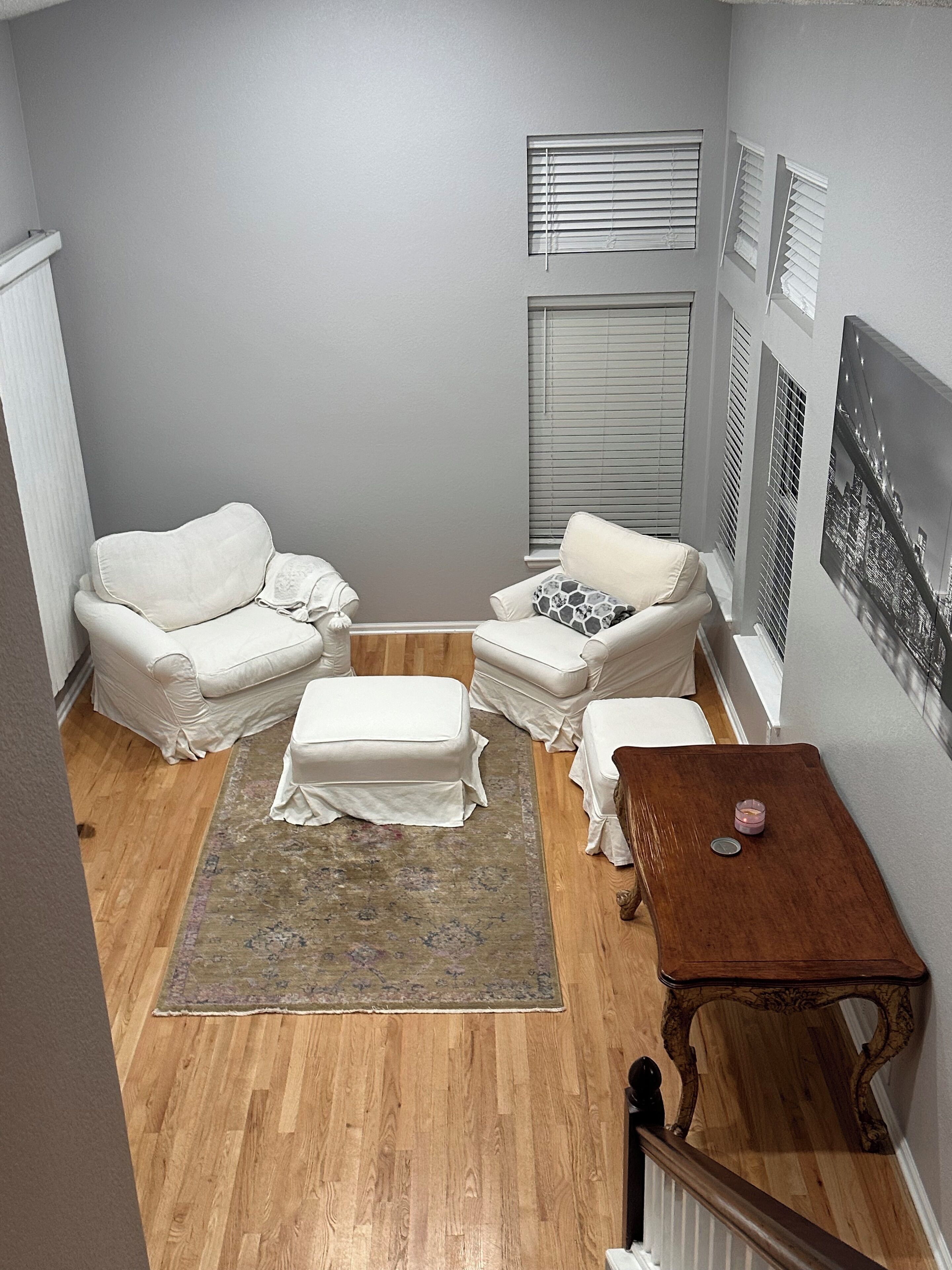 Una habitación con dos sillones blancos, un reposapiés a juego, una mesa de centro de madera y una alfombra estampada.