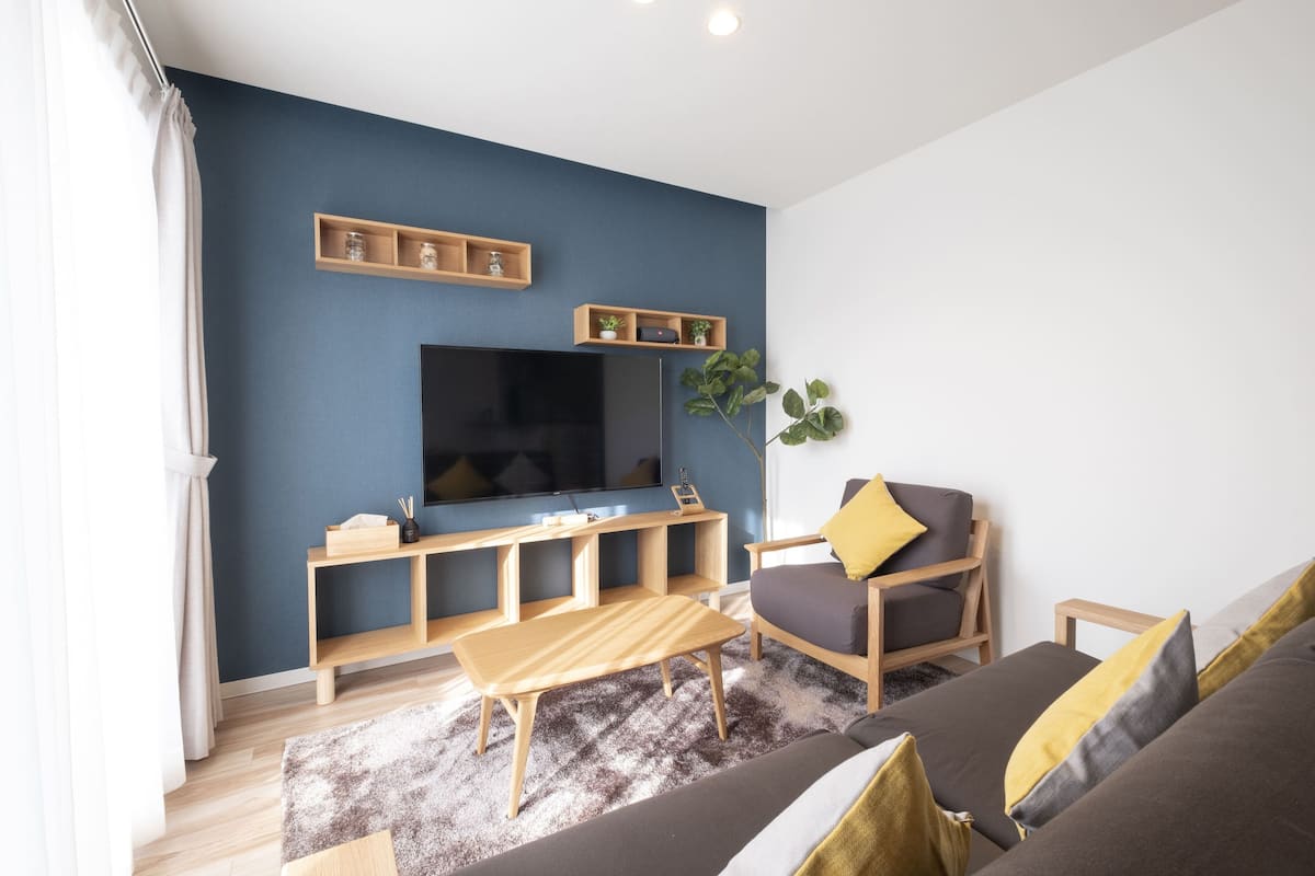 Una sala de estar moderna con un televisor de pantalla plana grande, muebles de madera y una planta.