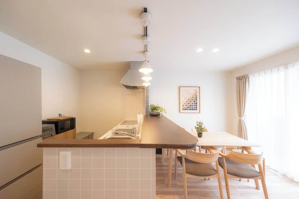 Una cocina moderna con una isla central, un comedor con mesa y sillas, y vistas al exterior a través de amplios ventanales.