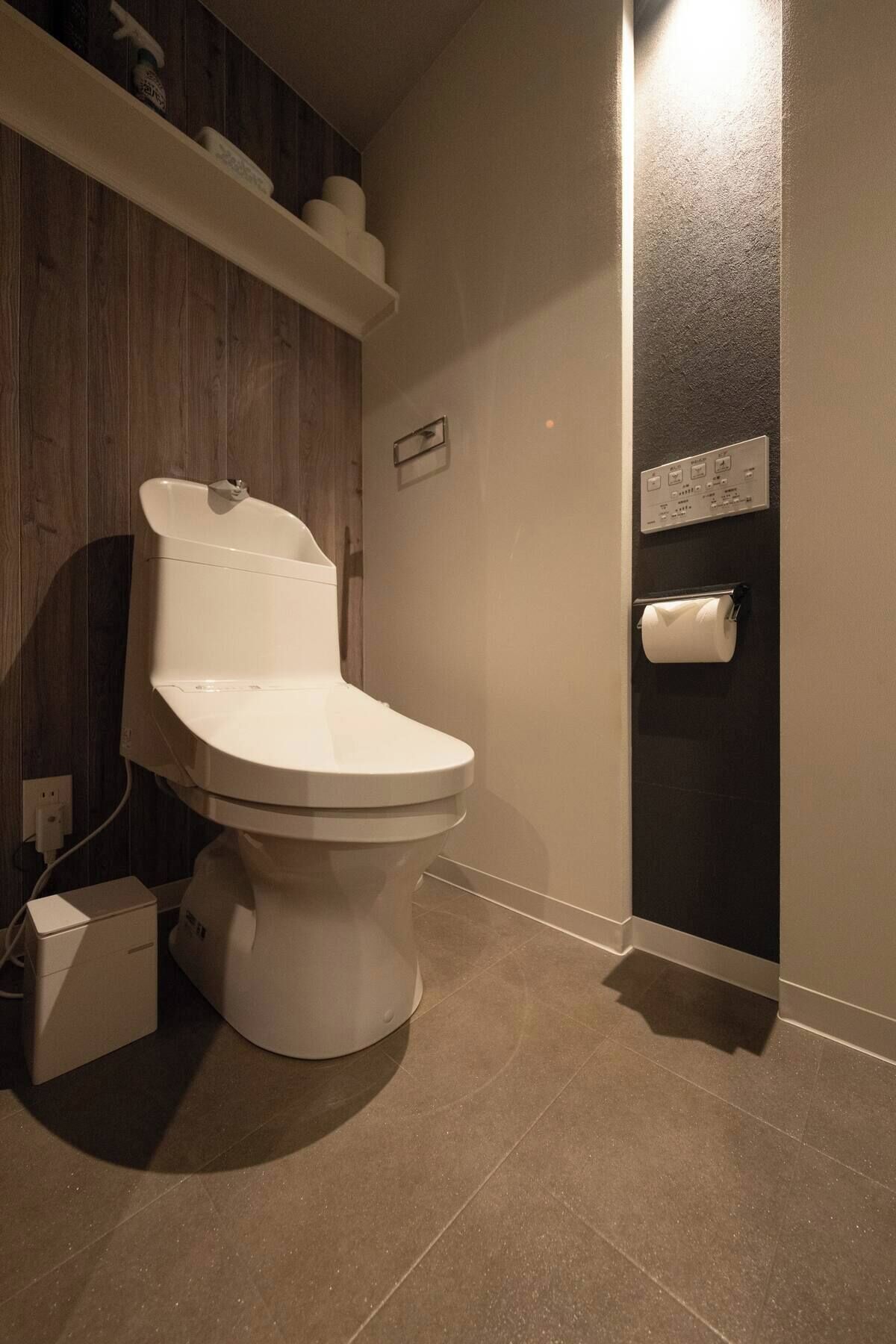 A modern bathroom with a white toilet, a wooden vanity, a towel rack, and a toilet paper holder on the wall.