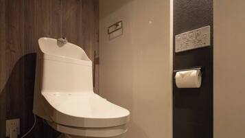 A modern bathroom with a white toilet, a wooden vanity, a towel rack, and a toilet paper holder on the wall.