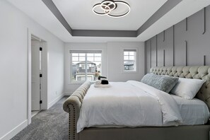 A bedroom with a large bed, a tufted headboard, and a modern light fixture.