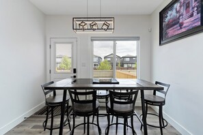 Un coin repas comprenant une table rectangulaire et quatre chaises, de grandes fenêtres et un tableau accroché au mur.