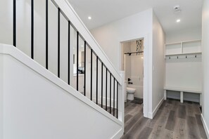 A modern interior with a staircase, a bathroom, and a hallway with built-in shelves. - Luxurious, Cozy, & Modern 4 bedroom Home—Airconditioned + Netflix + Free Parking (Edmonton)