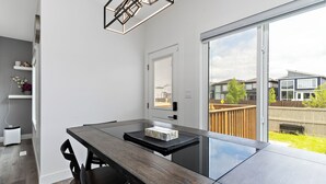 A modern kitchen with a large island, a dining area with a dark wooden table, and a sliding glass door leading to a backyard. - Luxurious, Cozy, & Modern 4 bedroom Home—Airconditioned + Netflix + Free Parking (Edmonton)