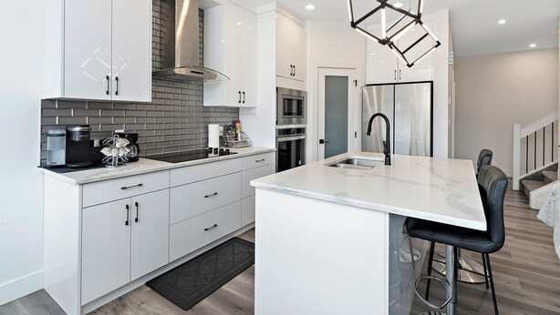 A modern kitchen with white cabinetry, a brick backsplash, stainless steel appliances, and a bar area with stools. - Luxurious, Cozy, & Modern 4 bedroom Home—Airconditioned + Netflix + Free Parking (Edmonton)