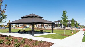 A pavilion with a roof and benches, surrounded by a well-maintained lawn and a sidewalk. - Luxurious, Cozy, & Modern 4 bedroom Home—Airconditioned + Netflix + Free Parking (Edmonton)
