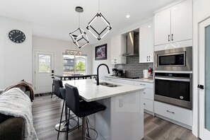 Une cuisine moderne dotée d’un îlot central, d’appareils électroménagers en acier inoxydable et de luminaires suspendus.
