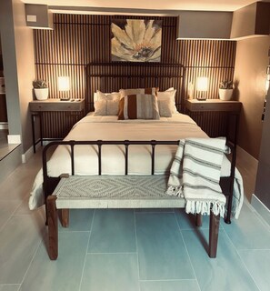 A modern bedroom with a large bed, a bench, two bedside tables with lamps, and a wall-mounted artwork. - Midtown 1BR Hideaway: Steps to Ice Blocks (Sacramento)