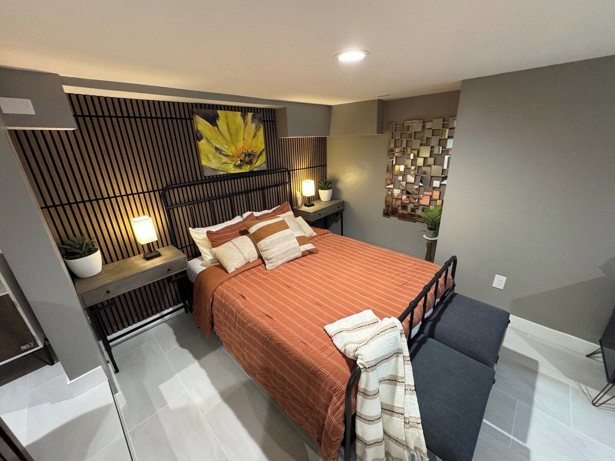 Un dormitorio moderno con cama, mesitas de noche, una obra de arte en la pared y un panel decorativo.