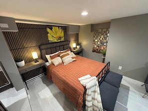 Un dormitorio moderno con cama, mesitas de noche, una obra de arte en la pared y un panel decorativo.