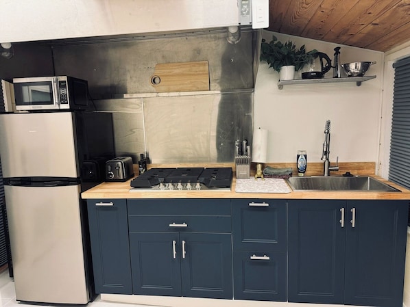 Una cocina compacta equipada con microondas, tostadora, estufa a gas, pileta y alacenas.