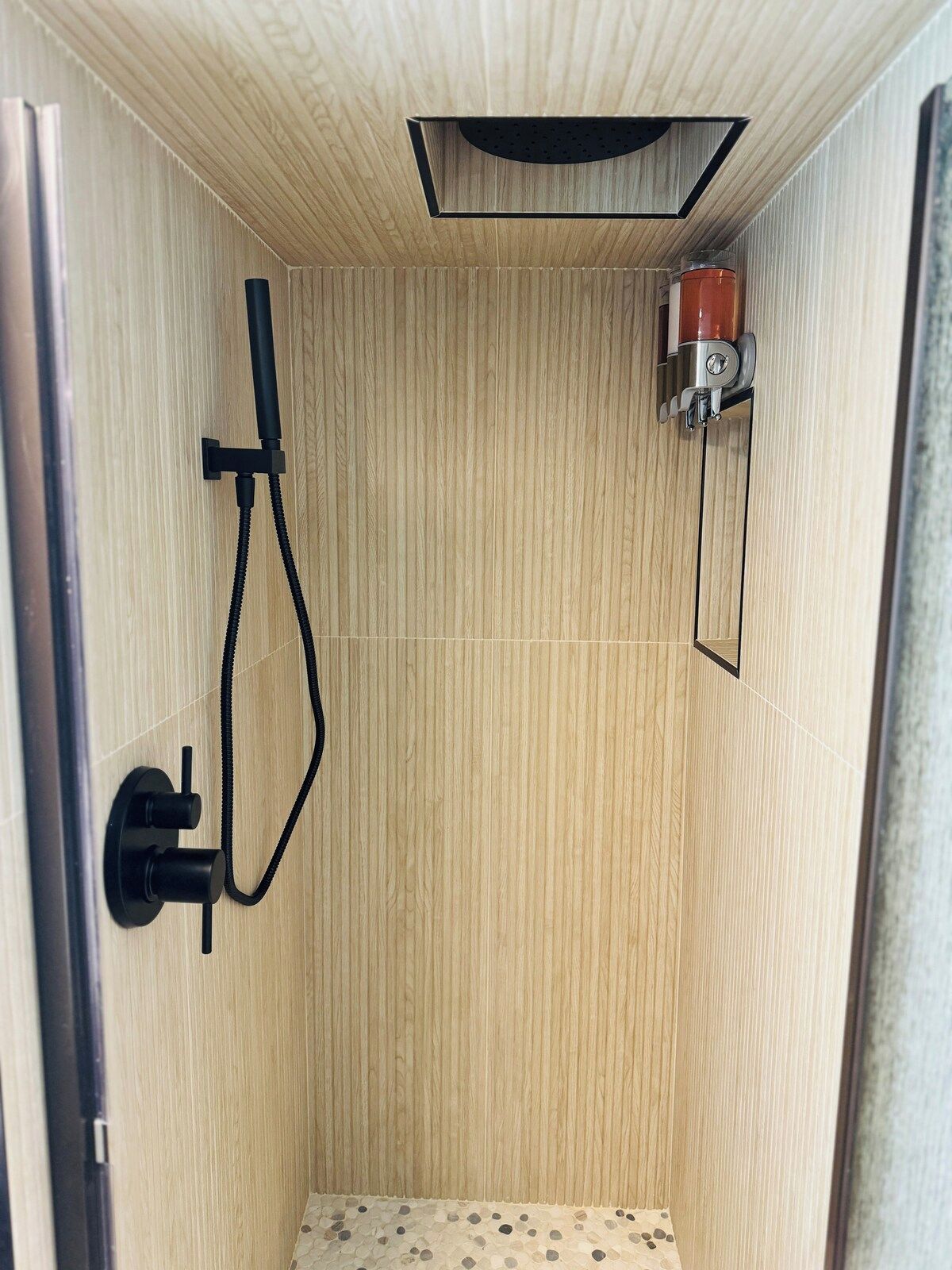 A shower with a wooden wall, a handheld showerhead, and a control unit.
