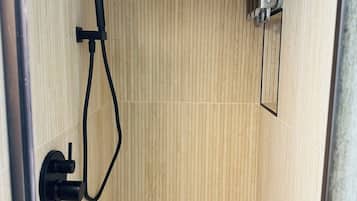 A shower with a wooden wall, a handheld showerhead, and a control unit.