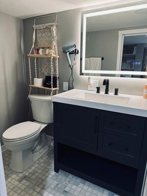 A bathroom with a toilet, a sink with a mirror, and a towel rack. - Midtown 1BR Hideaway: Steps to Ice Blocks (Sacramento)