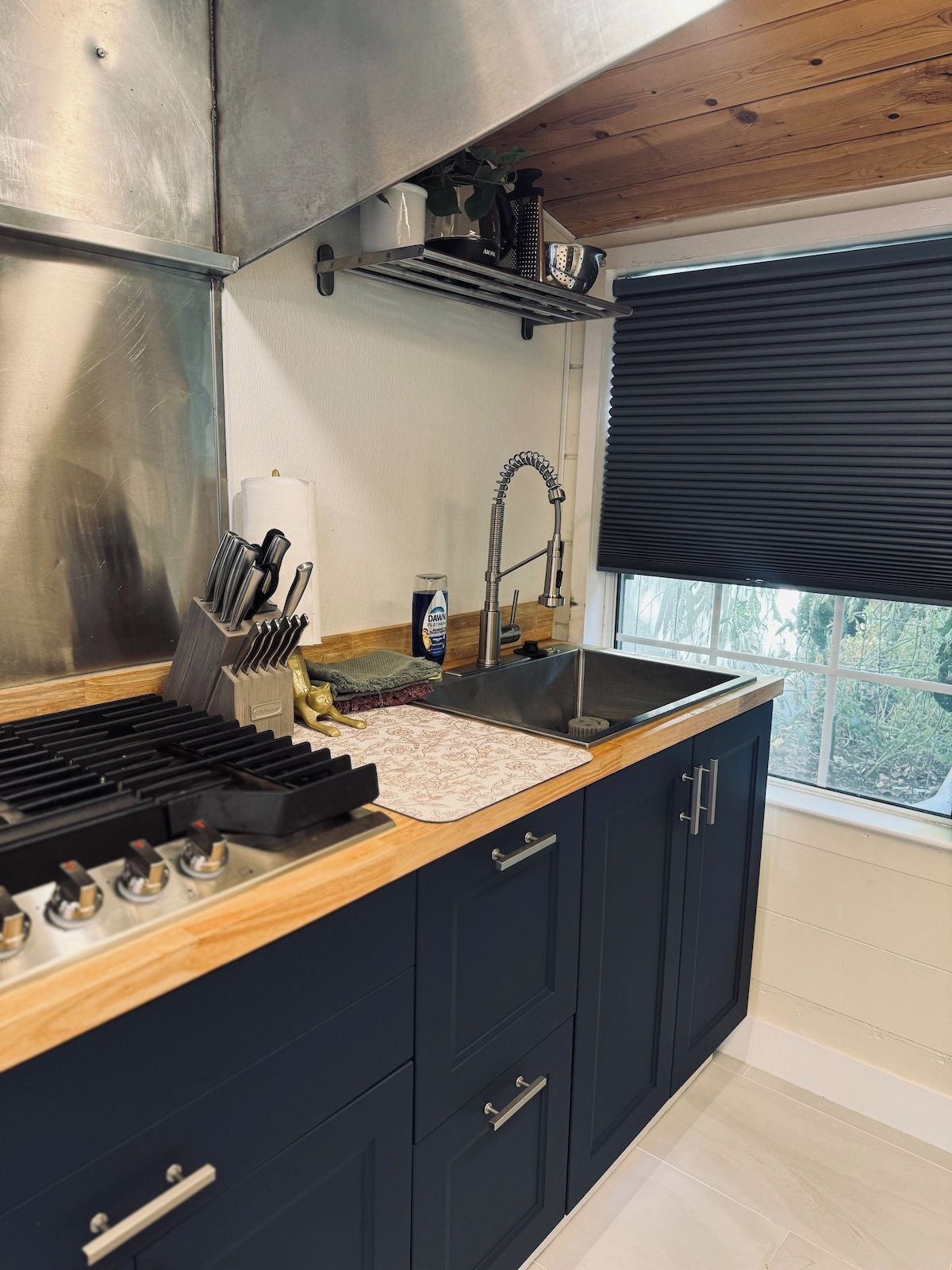 Una cocina moderna con extractor de acero inoxidable, pileta integrada y ventana con vista a follaje.