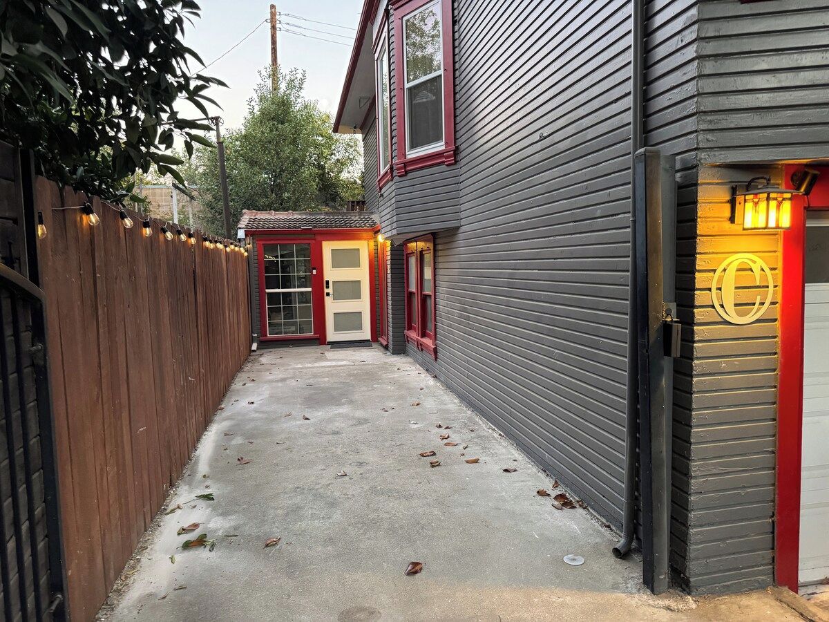 Une ruelle étroite, bordée d’une clôture en bois d’un côté et d’un immeuble avec une porte et des fenêtres rouges de l’autre.