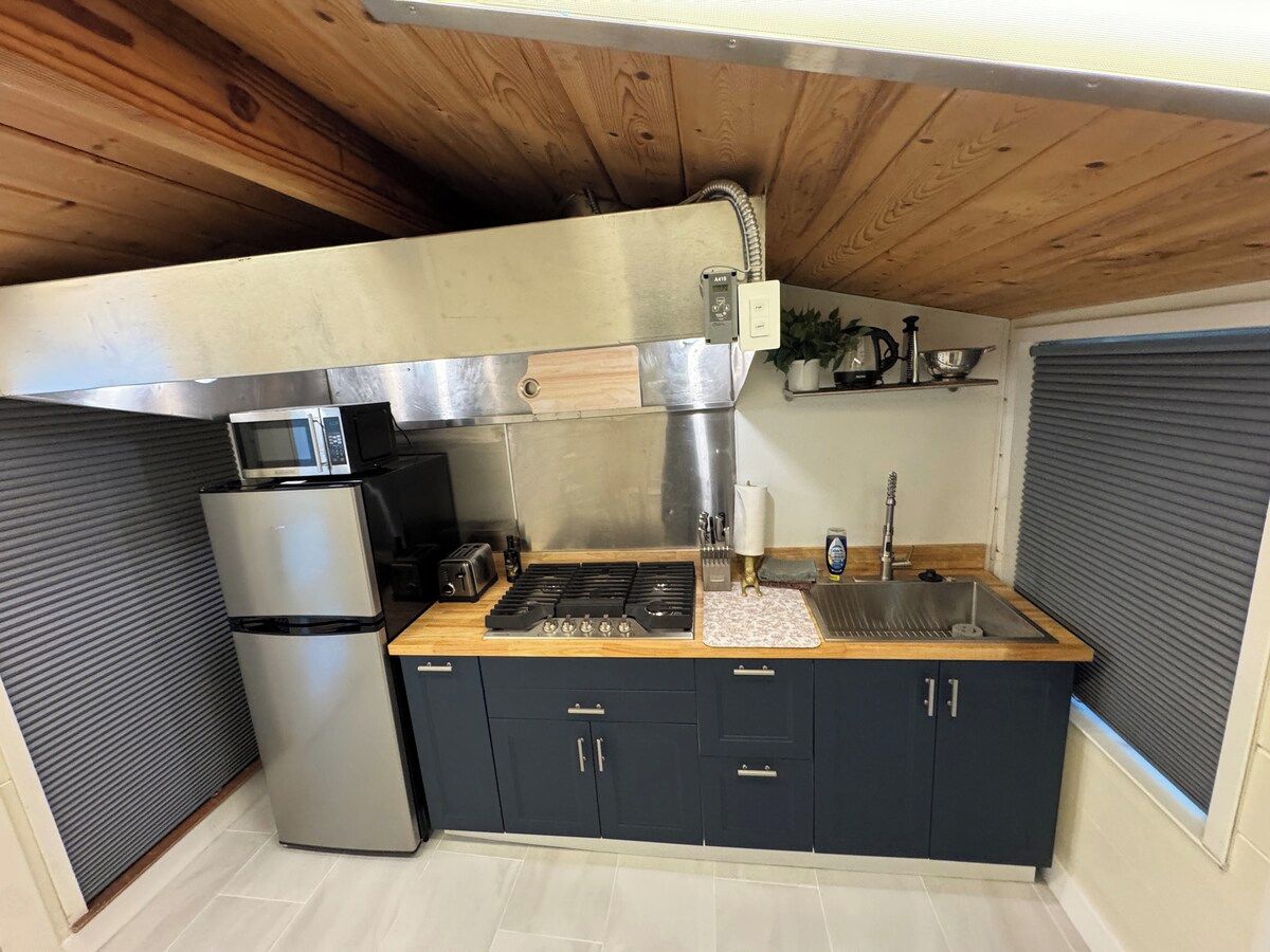 Una cocina compacta con estufa integrada, microondas y pileta, con alacenas oscuras y encimera de madera.