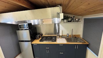 Una cocina compacta con estufa integrada, microondas y pileta, con alacenas oscuras y encimera de madera.