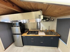 Una cucina compatta con piano cottura integrato, forno a microonde e lavello, caratterizzata da mobili scuri e un piano di lavoro in legno.