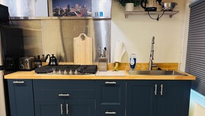 A modern kitchen with dark blue cabinets, a stainless steel range hood, a wooden countertop, and a black kettle. - Midtown Studio Hideaway: Steps to Ice Blocks (Sacramento)