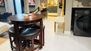 A modern living room with a round wooden table, black leather chairs, a small white chair, a dining table, and a kitchen area with a washing machine. - Midtown Studio Hideaway: Steps to Ice Blocks (Sacramento)